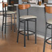 A group of Lancaster Table & Seating Boomerang Series bar stools with wooden backs and light gray vinyl seats.