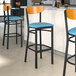 A group of Lancaster Table & Seating Boomerang Series bar stools with blue vinyl seats and cherry wood backs.