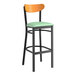 A Lancaster Table & Seating bar stool with a seafoam vinyl seat and cherry wood back and black frame.