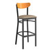 A Lancaster Table & Seating black bar stool with a tan vinyl seat and cherry wood back.