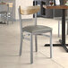 A Lancaster Table & Seating Boomerang chair with dark gray vinyl seat and driftwood back on a table in a restaurant.