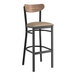 A Lancaster Table & Seating black bar stool with a wooden seat and taupe cushion.