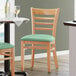 A Lancaster Table & Seating wooden chair with a seafoam vinyl cushion.