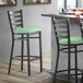 A Lancaster Table & Seating black ladder back bar stool with a seafoam green cushion.