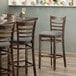 A Lancaster Table & Seating wood ladder back bar stool with a light gray vinyl seat on a table in a restaurant.