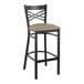 A black Lancaster Table & Seating bar stool with a taupe cushioned seat.