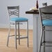 A Lancaster Table & Seating clear coat finish cross back bar stool with a blue vinyl padded seat and metal leg.