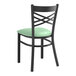 A black Lancaster Table & Seating metal cross back chair with a light green cushion.