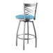 A Lancaster Table & Seating clear coat finish cross back swivel bar stool with a blue vinyl padded seat.