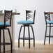A Lancaster Table & Seating black metal swivel bar stool with a blue cushion.
