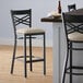A Lancaster Table & Seating black cross back bar stool with a light gray cushion on the seat.