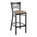 A black Lancaster Table & Seating cross back bar stool with a taupe cushion.