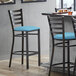 A Lancaster Table & Seating ladder back bar stool with a blue vinyl cushion on a white surface.