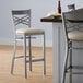 A Lancaster Table & Seating clear coat finish cross back bar stool with a light gray vinyl padded seat.