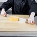 A person using a Dexter-Russell double wooden handled cheese knife to cut cheese on a cutting board.