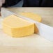 A person using a Dexter-Russell cheese knife to cut cheese on a counter.