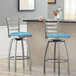Two Lancaster Table & Seating clear coat finish ladder back swivel bar stools with blue vinyl padded seats at a counter.