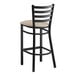 A black Lancaster Table & Seating ladder back bar stool with a light gray padded seat.