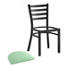 A black Lancaster Table & Seating ladder back chair with a seafoam green vinyl padded seat.