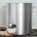 A person holding a spoon over a Vollrath Classic Aluminum stock pot.