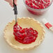 A person using a spoon to spread Rich's Allen Red Cherry pie filling in a pie.