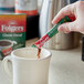 A person pouring Folgers Classic Decaf Instant Coffee from a green packet into a white mug.