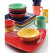 A stack of Tuxton Concentrix Cinnebar square bowls and plates in red, yellow, and green.