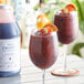 A bottle of Narvon Sangria Frozen Cocktail Mix with two wine glasses filled with sangria, one garnished with fruit.