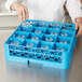 A woman using a Carlisle blue plastic OptiClean glass rack with extenders to wash wine glasses.