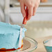 A hand holding a Choice offset baking / icing spatula with a wood handle over a blue cake.