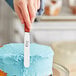 A hand using a Choice baking spatula to cut a blue cake.
