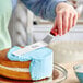 A person using a Choice offset spatula with a wood handle to spread blue frosting on a cake.