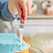 A person using a Choice offset baking spatula with blue frosting on a cake.
