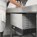 A person standing at a counter in a school kitchen with a Hatco booster heater on it.