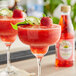 Two glasses of strawberry margaritas garnished with strawberries on a table with a bottle of Rose's Strawberry Syrup.