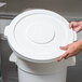 A person holding a white plastic lid for a Continental Huskee trash can.
