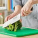 A person using a Choice Classic Santoku Knife to cut broccoli on a green cutting board.