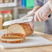 A person cutting a loaf of bread with a Choice Classic serrated bread knife.