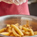 A gloved hand pouring Morton Sea Salt into a bowl of french fries.