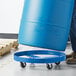 A man using a Lavex steel drum dolly to move a blue drum.