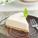A slice of Daiya plain vegan cheesecake with a leaf of mint on a white plate with a fork.