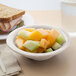 A Carlisle bone rimmed melamine bowl filled with fruit and a sandwich.