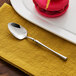 An Acopa Hepburn stainless steel teaspoon on a plate with a pink macaroon.