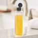 A clear plastic Cylinder 8 oz. bottle of orange liquid with a black flip top lid on a kitchen counter.