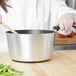A woman using a Vollrath Wear-Ever sauce pan with a black silicone handle to cook vegetables.