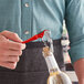 A person using an Acopa red metal waiter's corkscrew to open a bottle of wine.