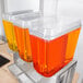 A stainless steel Crathco refrigerated beverage dispenser with three containers of orange and yellow liquid.