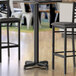 A black Lancaster Table & Seating bar table base with two chairs.