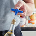 A hand using a Choice blue plastic pocket corkscrew to open a bottle of wine.