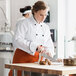 A woman in a Uncommon Chef white chef coat with black piping cutting potatoes.